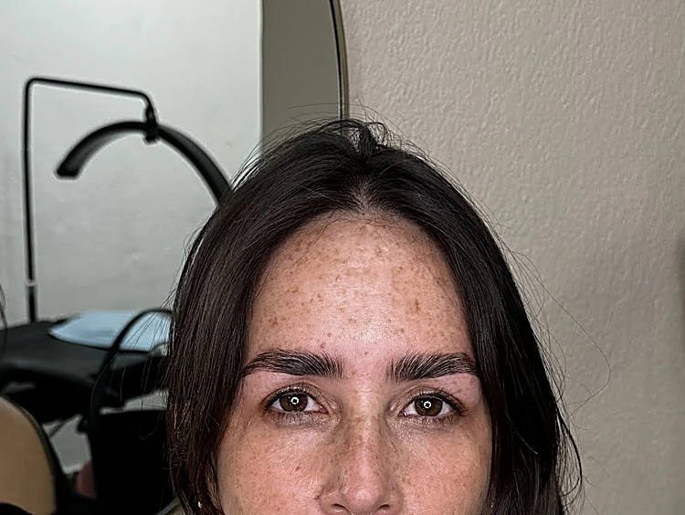 Clienta con pecas y cejas rectas y pobladas, frente a un espejo redondo del local.