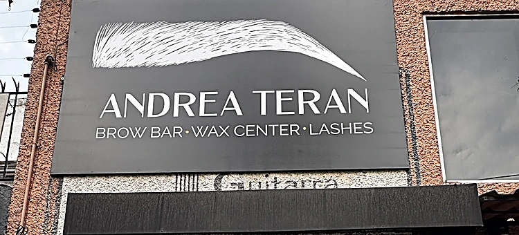 Letrero negro de la fachada con la ceja dibujada en trazos blancos sobre el nombre Andrea Terán y la línea Brow Bar, Wax Center, Lashes.