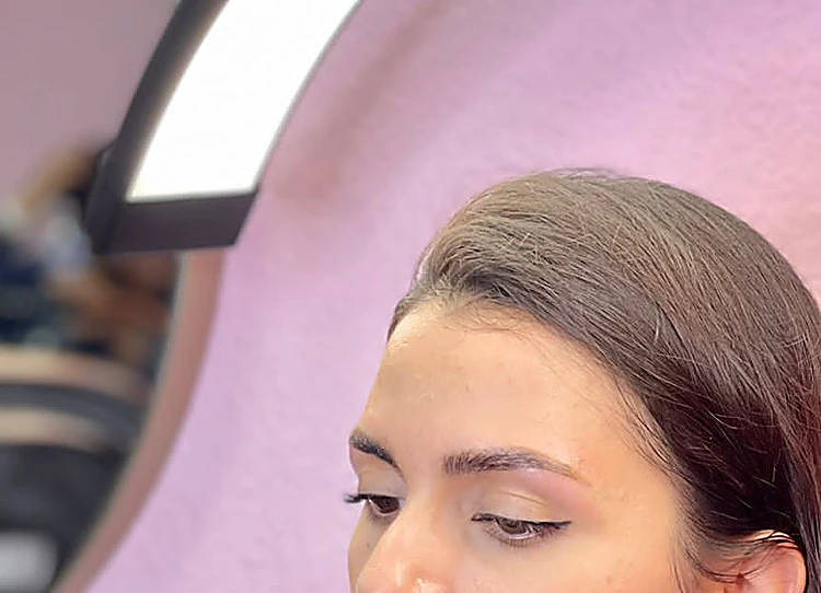 Clienta de perfil mirándose en el espejo con su ceja recién diseñada, junto a la lámpara de aro y el muro rosa.
